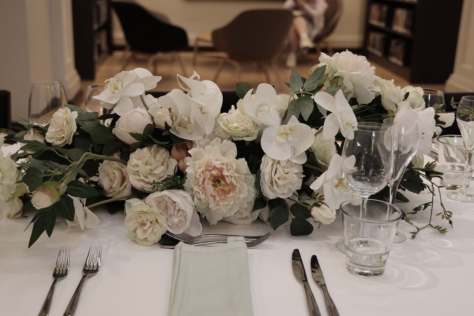 Mesa posta com toalha branca, taças e um arranjo baixo de rosas brancas